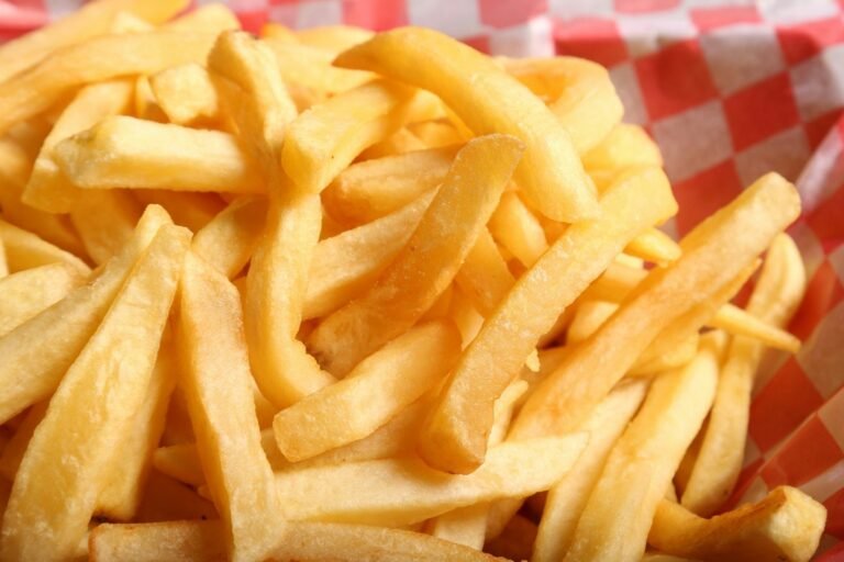 Basket of crispy golden french fries piled together on a red checkered paper liner